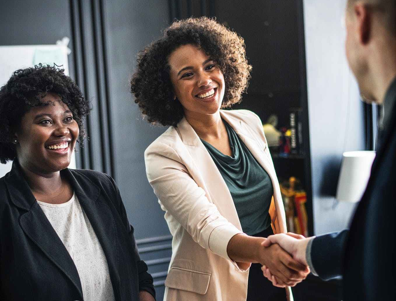 woman wears beige suit hand shaking man wear suit